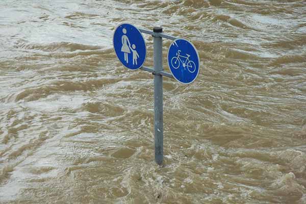 Flood waters somewhere flowing past a street warning signs for pedestrians and cyclists