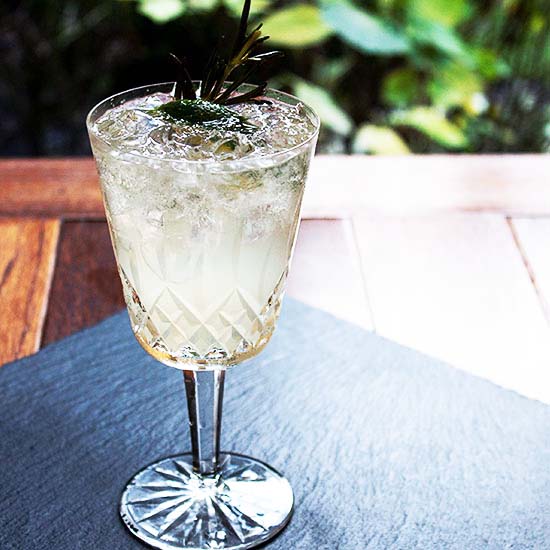 A Tailor At Home Cocktail with a wedge of lime and syrup infused sprig of rosemary