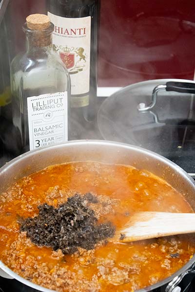 bolognese simmering in pan with some minced black olives ready to be stir in